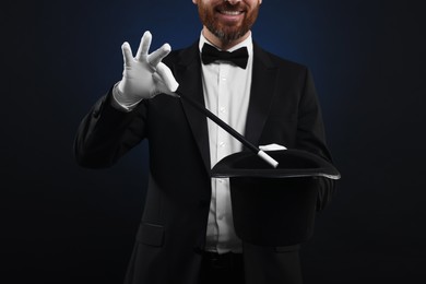 Photo of Magician showing magic trick with top hat on dark blue background, closeup
