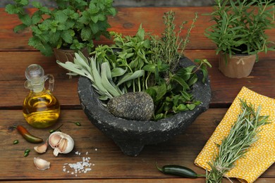 Photo of Mortar, different herbs, vegetables and oil on wooden table