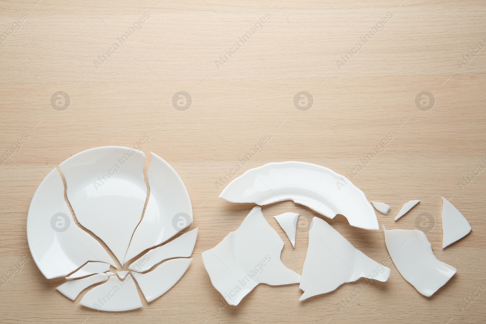 Photo of Two broken ceramic plates on wooden table, flat lay. Space for text