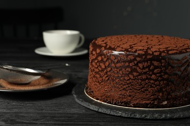 Photo of Delicious chocolate truffle cake and cocoa powder on black wooden table