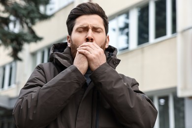 Sick man coughing on city street. Cold symptoms