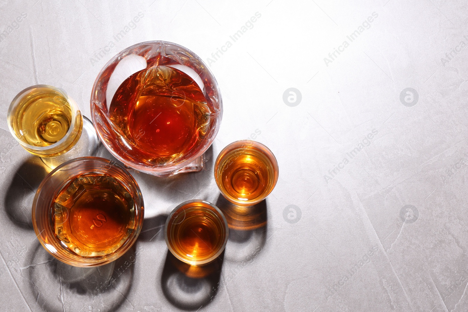 Photo of Many different liqueurs in glasses on light table, flat lay. Space for text