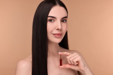 Beautiful young woman holding skincare ampoule on beige background