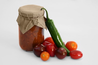 Jar with delicious salsa sauce and ingredients on white background
