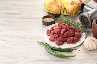 Photo of Pieces of beef, metal meat grinder and products on white wooden table. Space for text