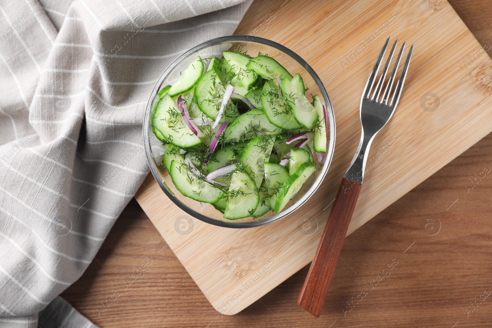 Photo of Bowl of tasty cucumber salad served on wooden table, flat lay