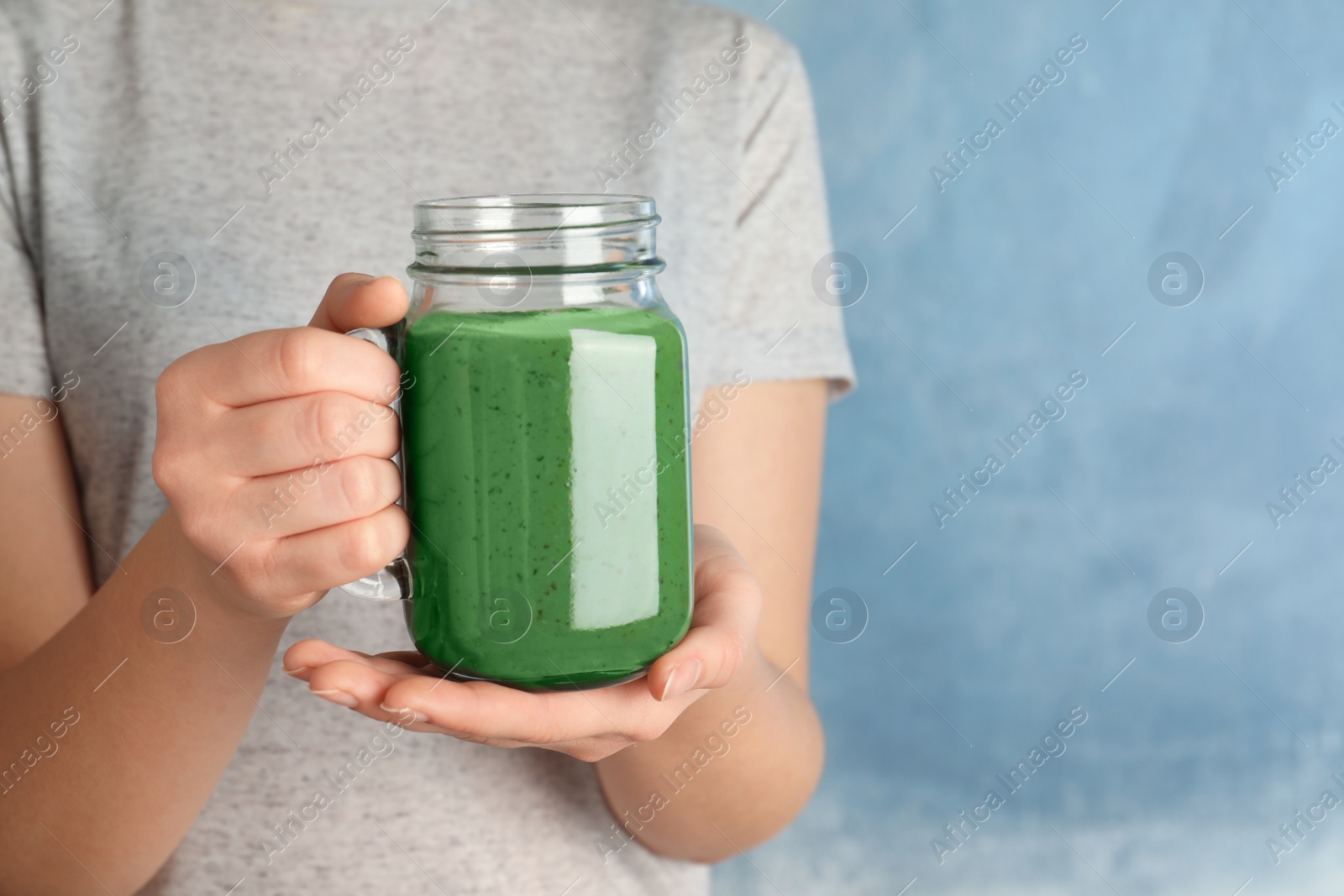 Photo of Woman holding mason jar of spirulina smoothie on color background, closeup. Space for text