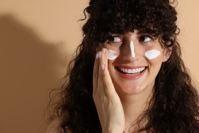 Photo of Beautiful young woman applying sun protection cream onto face on beige background, space for text