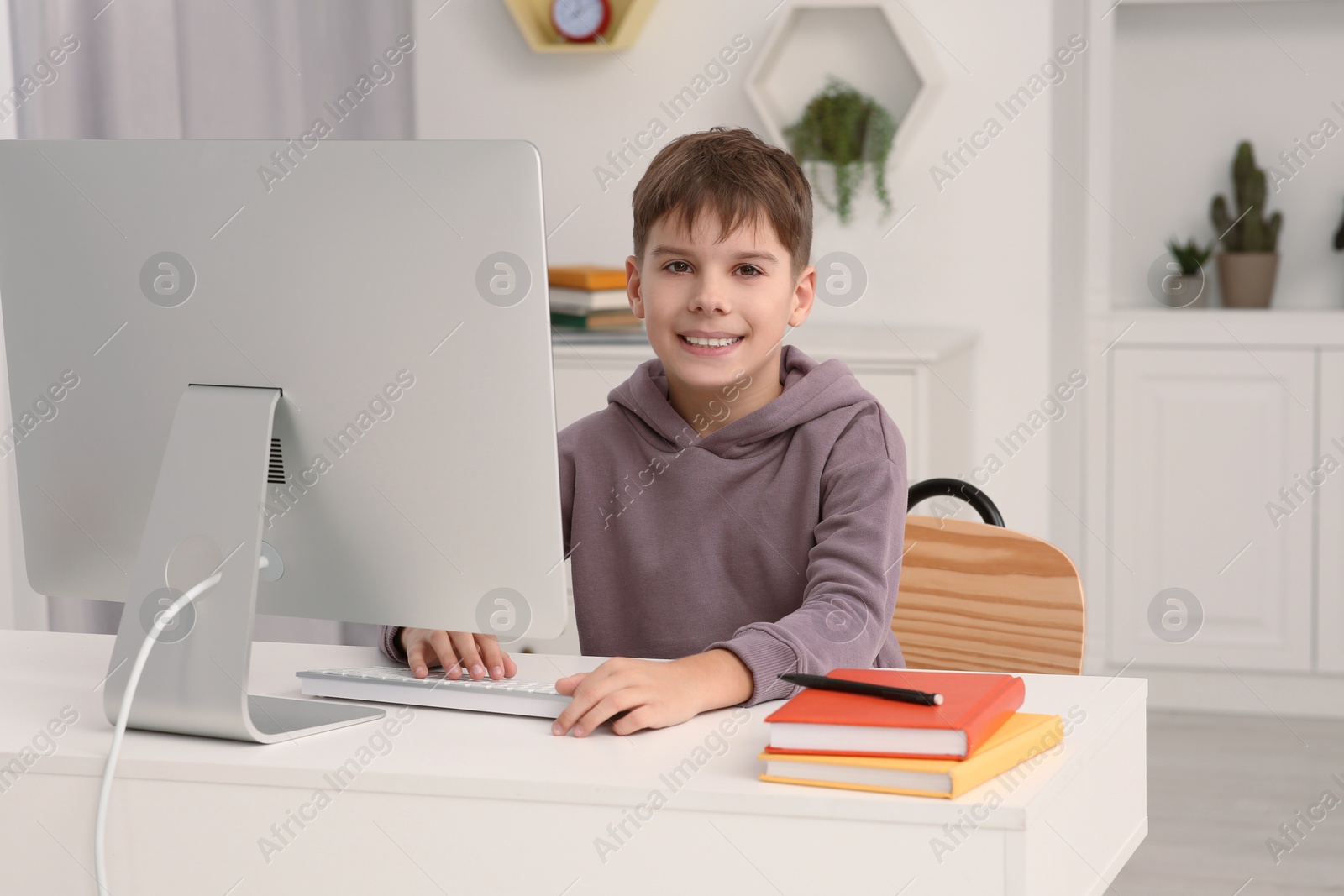 Photo of Boy using computer at desk in room. Home workplace