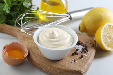 Tasty mayonnaise sauce in bowl, ingredients and spices on white table, closeup