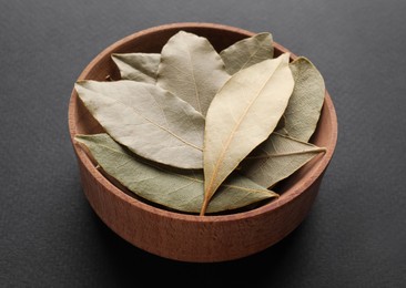 Bay leaves in wooden bowl on grey background