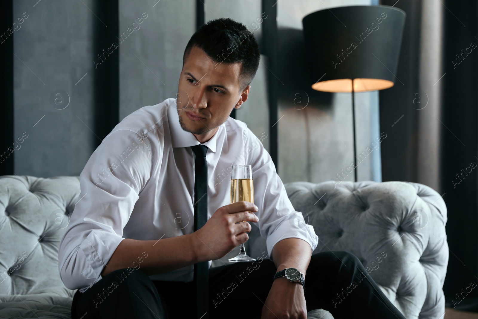 Photo of Handsome businessman with glass of champagne on sofa indoors. Luxury lifestyle