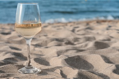 Photo of Glasstasty wine on sand near sea, space for text