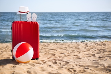 Bright suitcase and different beach accessories on sand near sea. Space for text