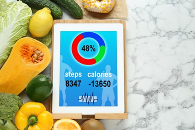 Tablet with weight loss calculator application and food products on white marble table, flat lay. Space for text