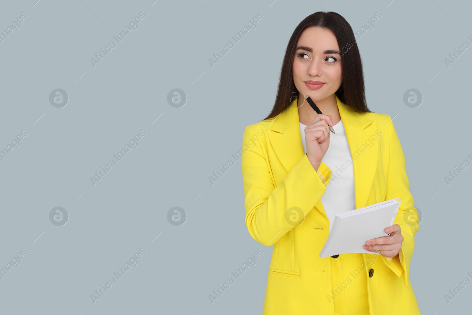 Photo of Young female intern with pen and notebook on grey background, space for text