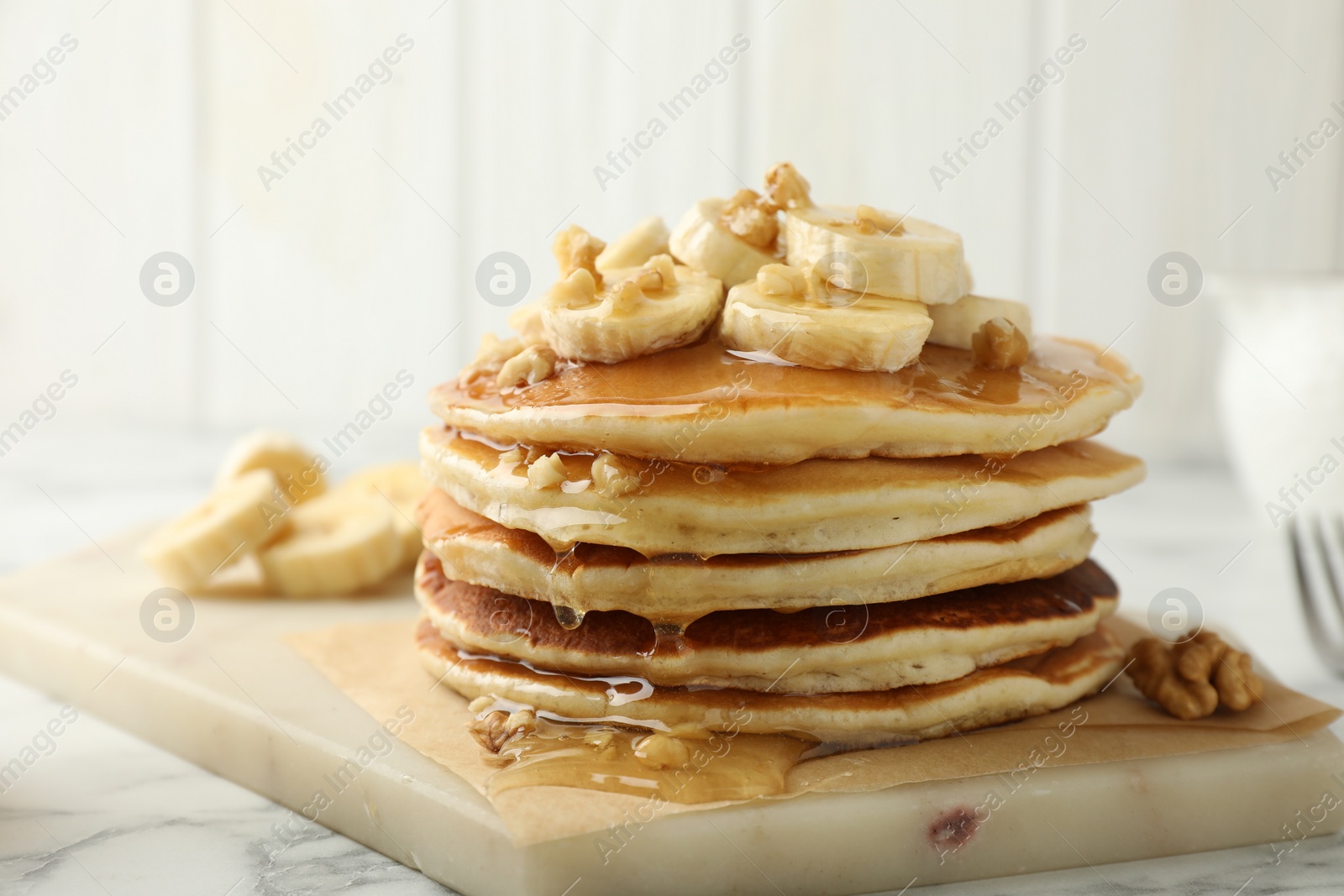 Photo of Delicious pancakes with bananas, walnuts and honey on white marble table, closeup