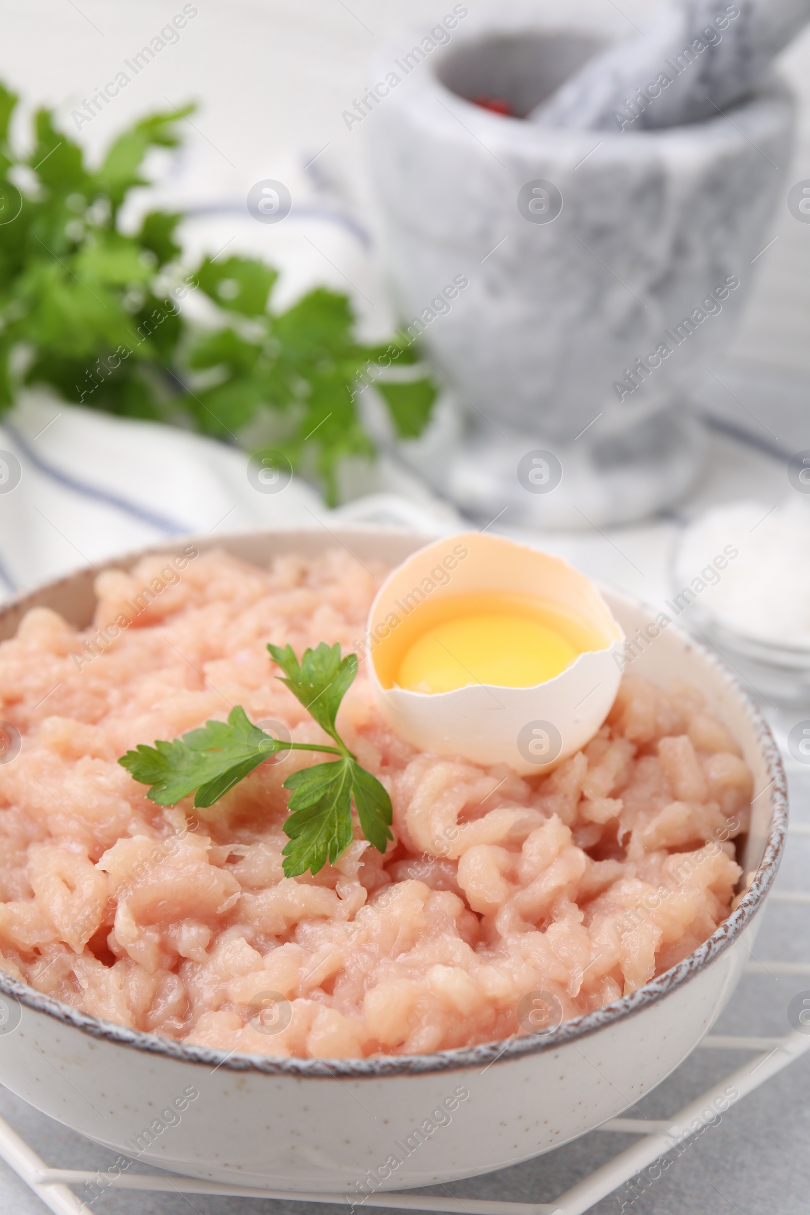 Photo of Fresh raw minced meat, parsley and egg in bowl on light grey table, closeup