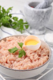 Photo of Fresh raw minced meat, parsley and egg in bowl on light grey table, closeup