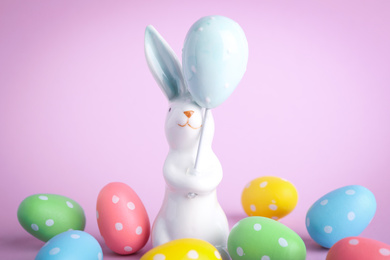 Easter bunny figure and dyed eggs on violet background