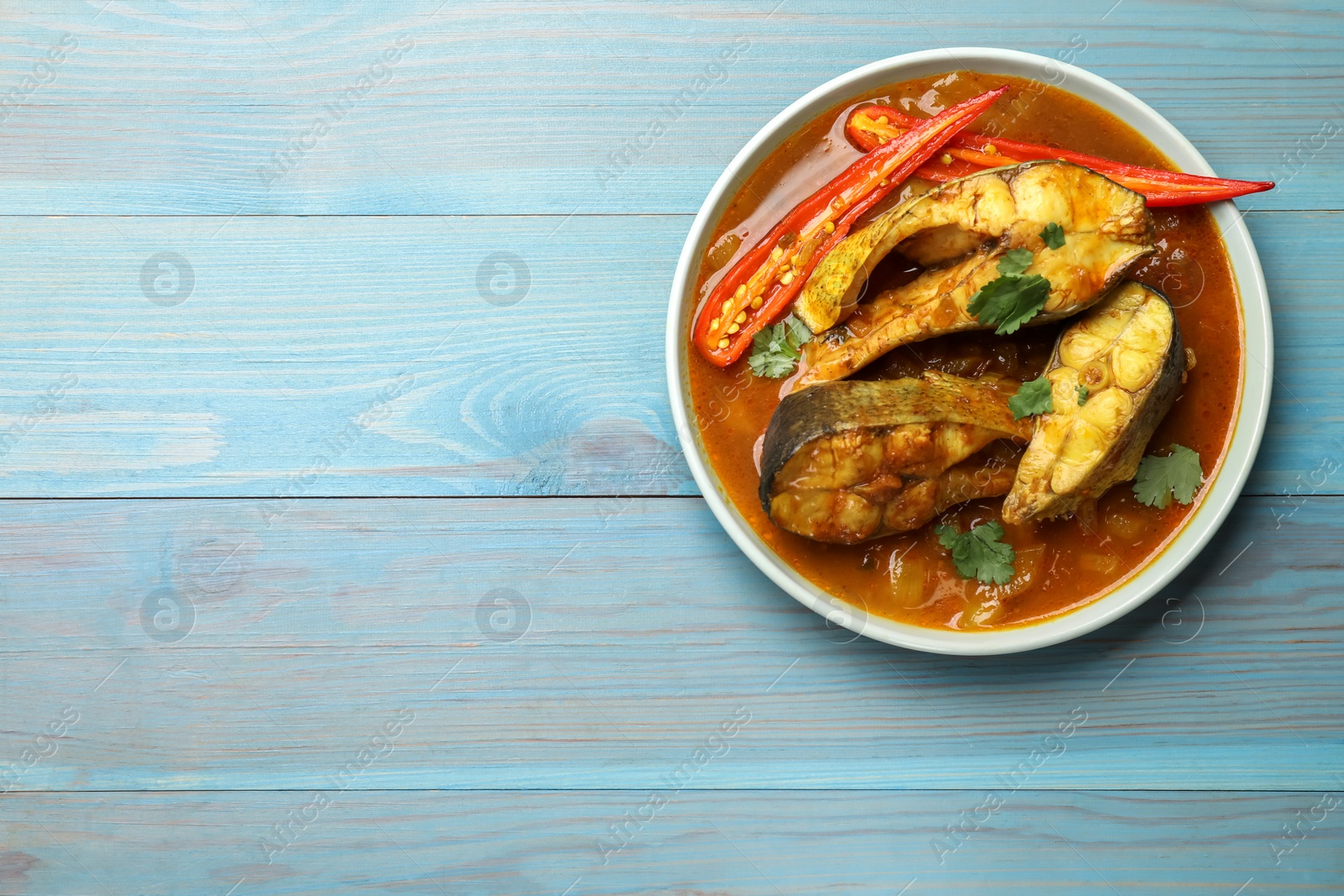 Photo of Tasty fish curry on light blue wooden table, top view. Space for text. Indian cuisine