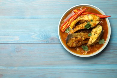 Photo of Tasty fish curry on light blue wooden table, top view. Space for text. Indian cuisine