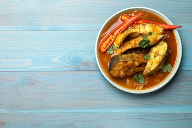 Tasty fish curry on light blue wooden table, top view. Space for text. Indian cuisine