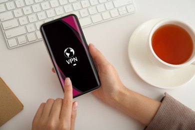 Image of Woman using smartphone with switched on VPN at white table, top view
