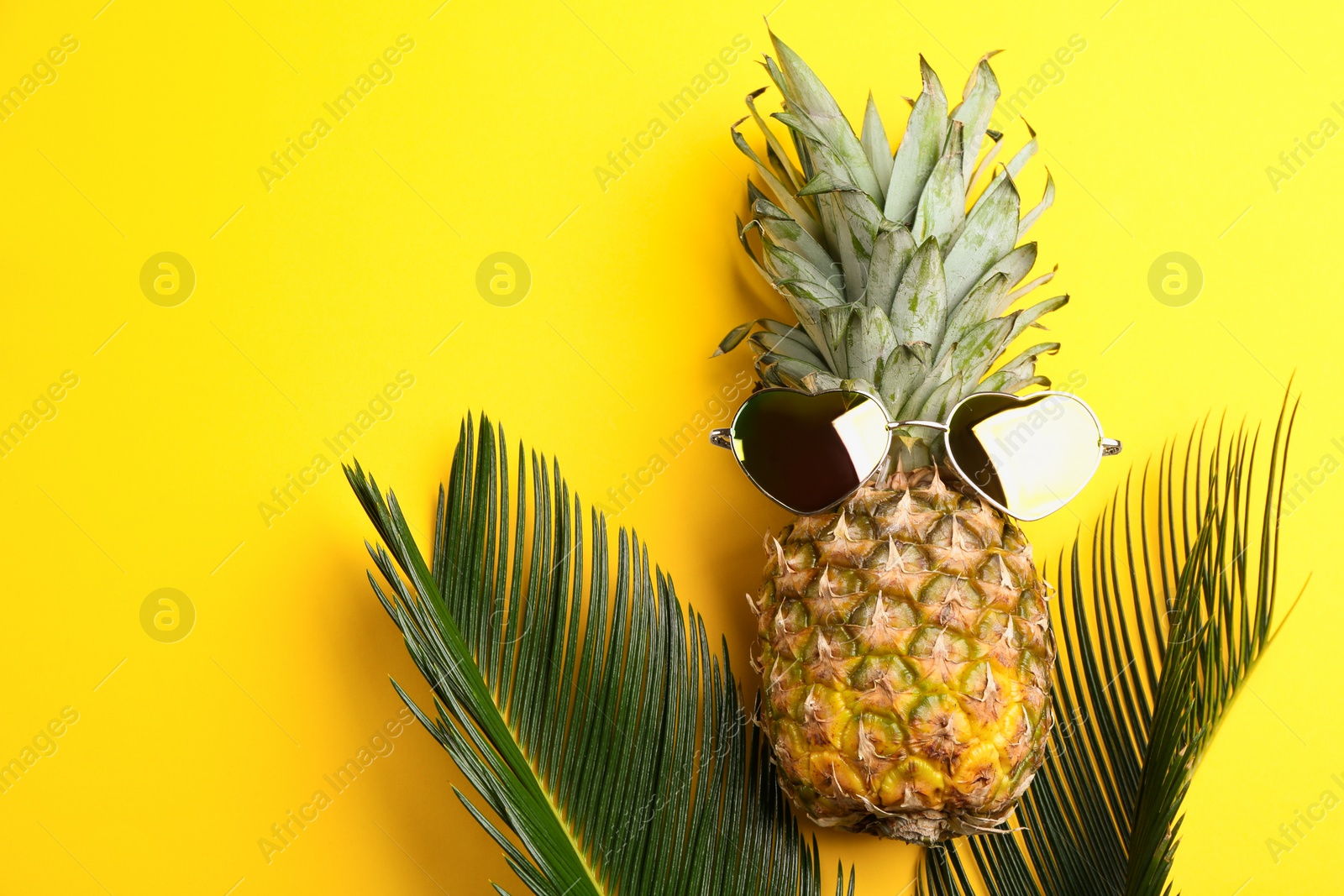 Photo of Pineapple with sunglasses and palm leaves on yellow background, flat lay