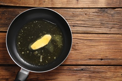 Photo of Melting butter in frying pan on wooden table, top view. Space for text