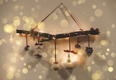 Beautiful Christmas decoration of tree branch, fairy lights and holiday ornaments hanging on wall, bokeh effect