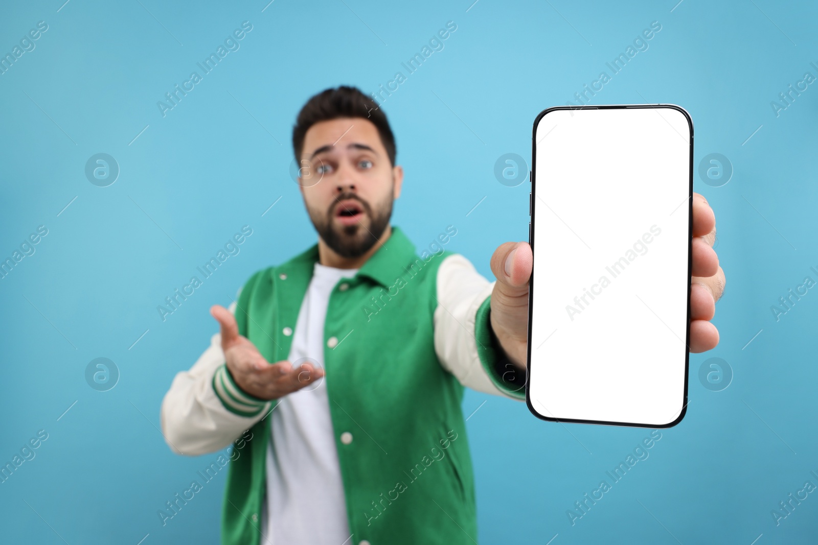 Photo of Surprised man showing smartphone in hand on light blue background, selective focus. Mockup for design