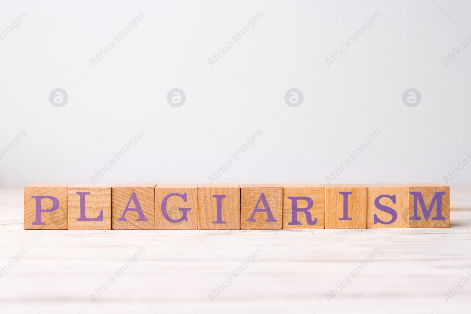 Photo of Wooden cubes with word Plagiarism on white table, space for text