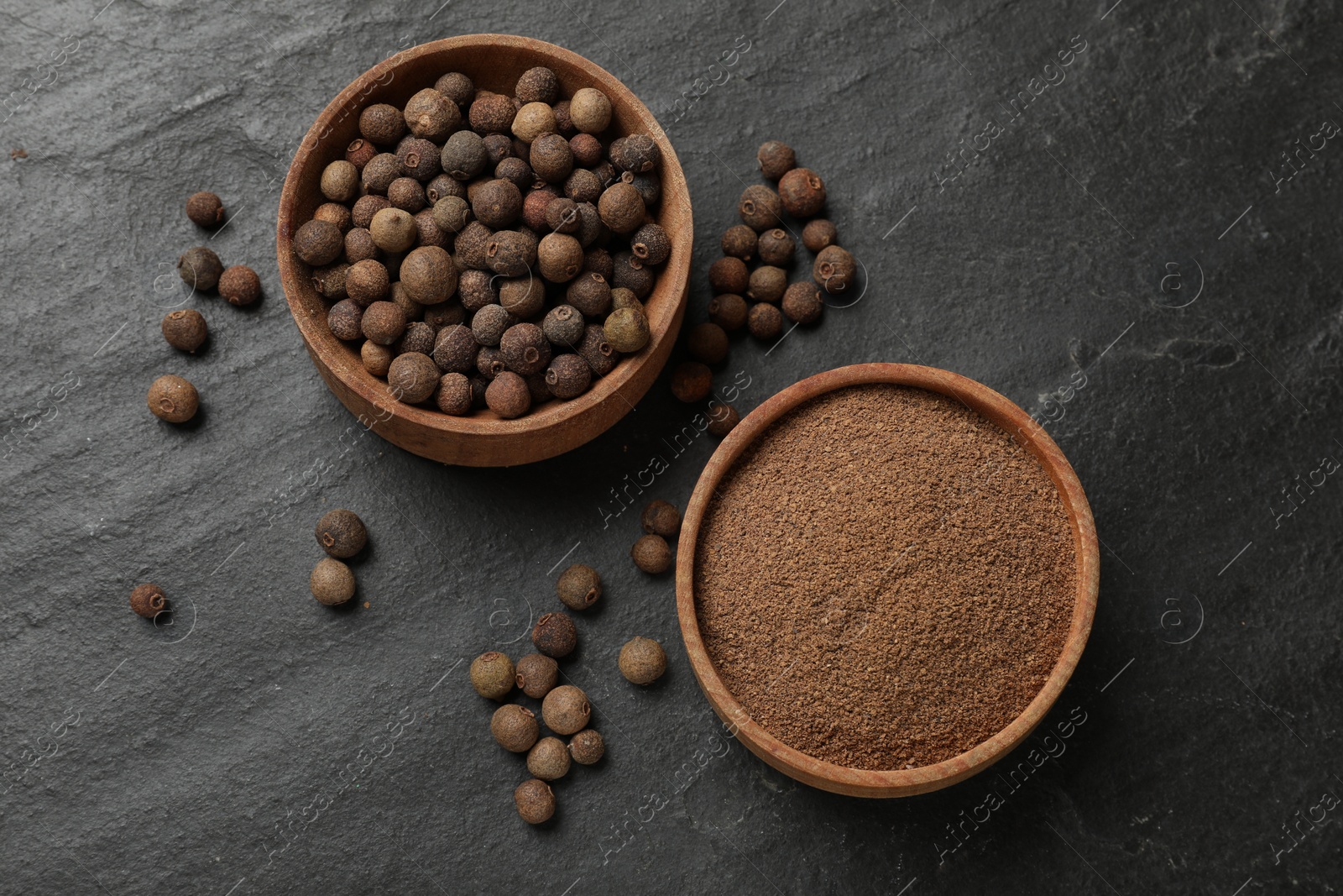 Photo of Ground and whole allspice berries (Jamaica pepper) on black table, top view