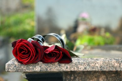 Red roses on grey tombstone outdoors, space for text. Funeral ceremony