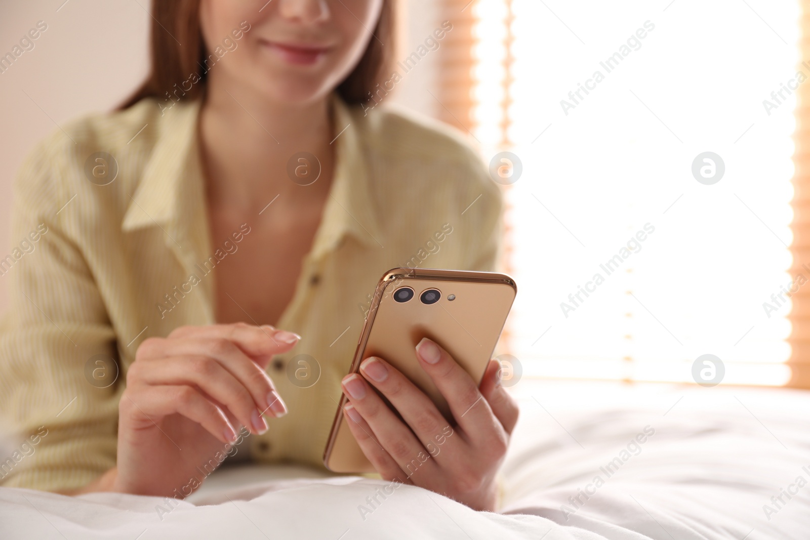 Photo of Young woman using modern smartphone on bed at home, closeup