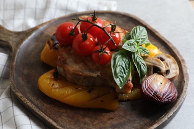 Photo of Serving board with tasty grilled meat and vegetables on light table, closeup