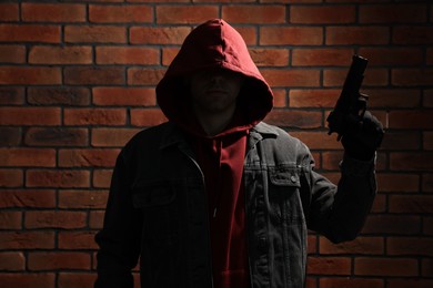 Photo of Thief in hoodie with gun against red brick wall