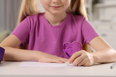 Photo of Girl erasing mistake in her homework at white desk in room, closeup