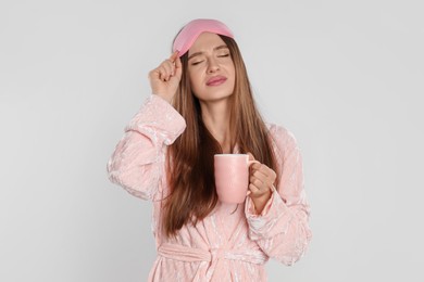 Photo of Beautiful young woman in bathrobe with cup of coffee on light background