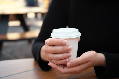 Photo of Woman with cardboard cup of coffee at table outdoors, closeup