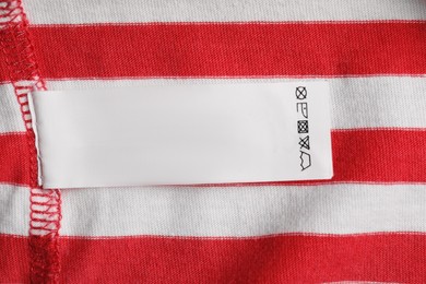 Photo of Clothing label with recommendations for care on striped garment, top view