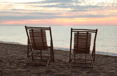 Wooden deck chairs on sandy beach at sunset. Summer vacation