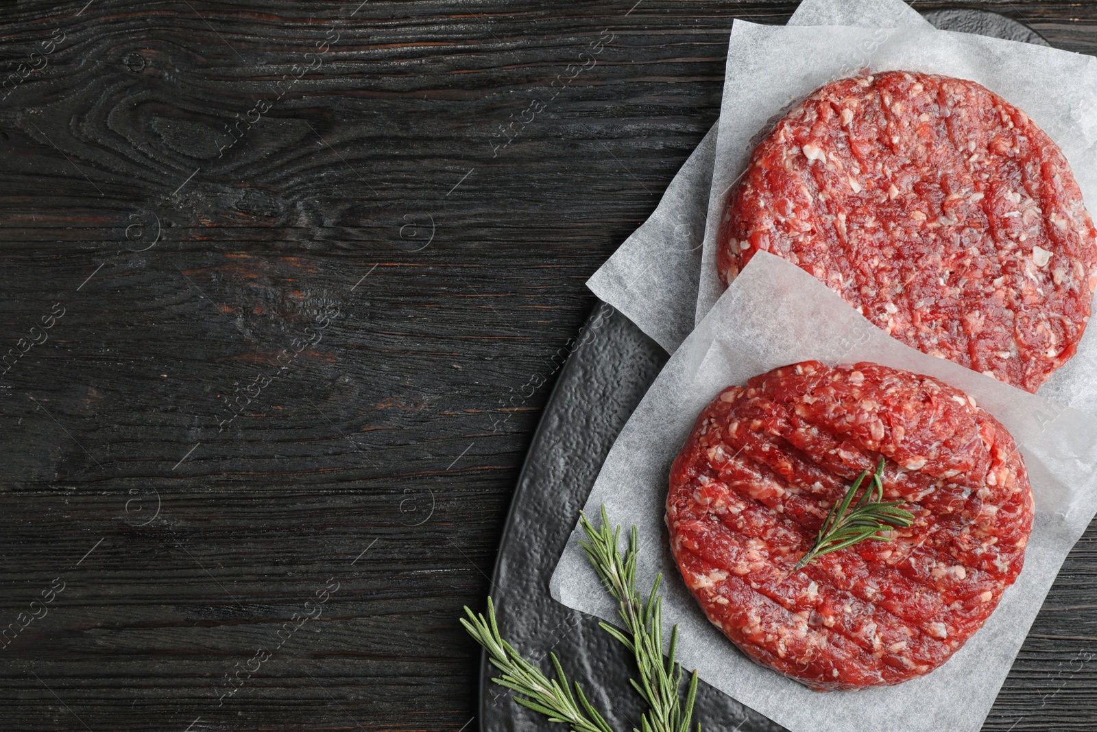 Photo of Raw meat cutlets for burger on black wooden table, top view. Space for text