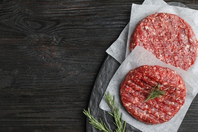 Photo of Raw meat cutlets for burger on black wooden table, top view. Space for text