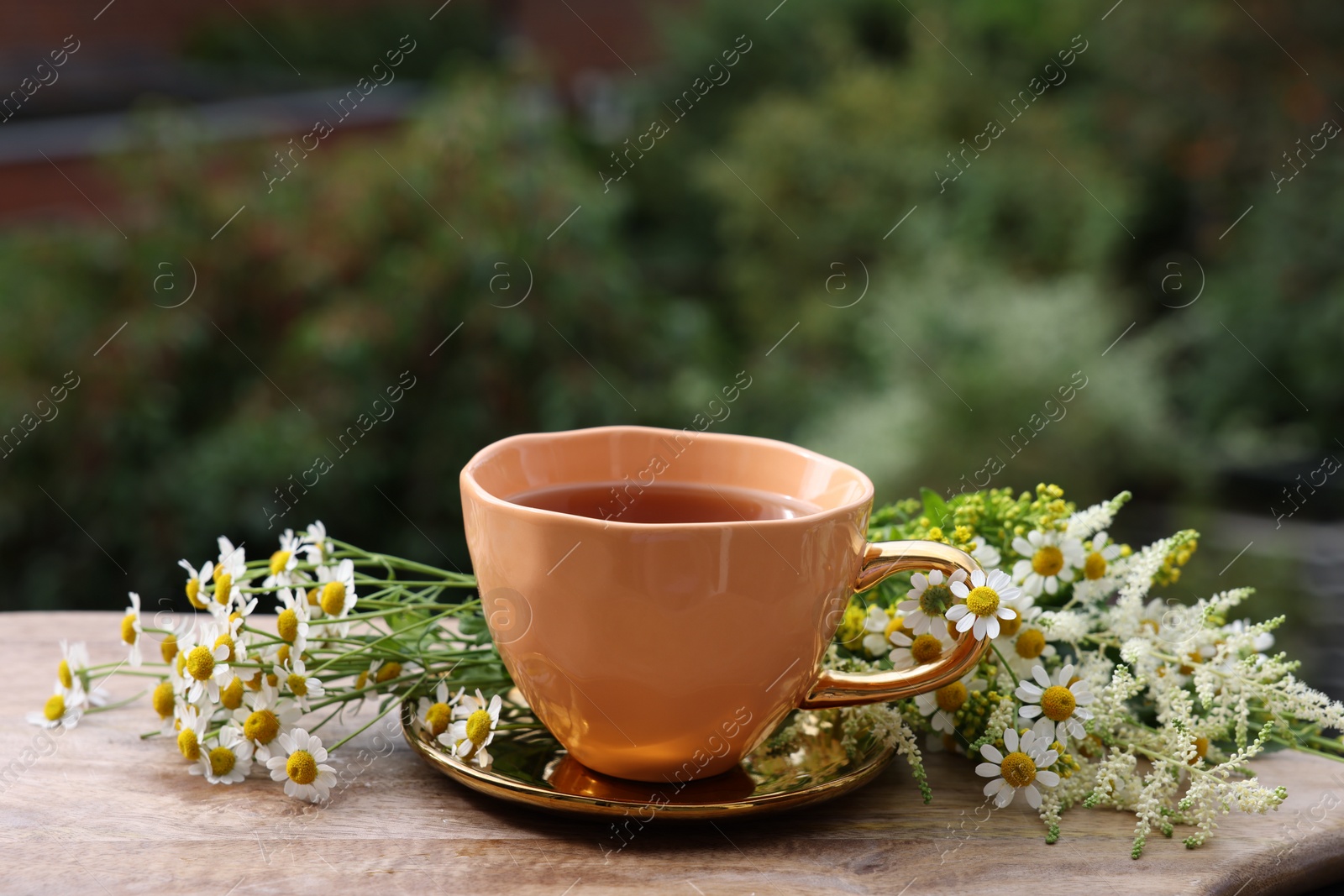 Photo of Cup of delicious chamomile tea and fresh flowers outdoors