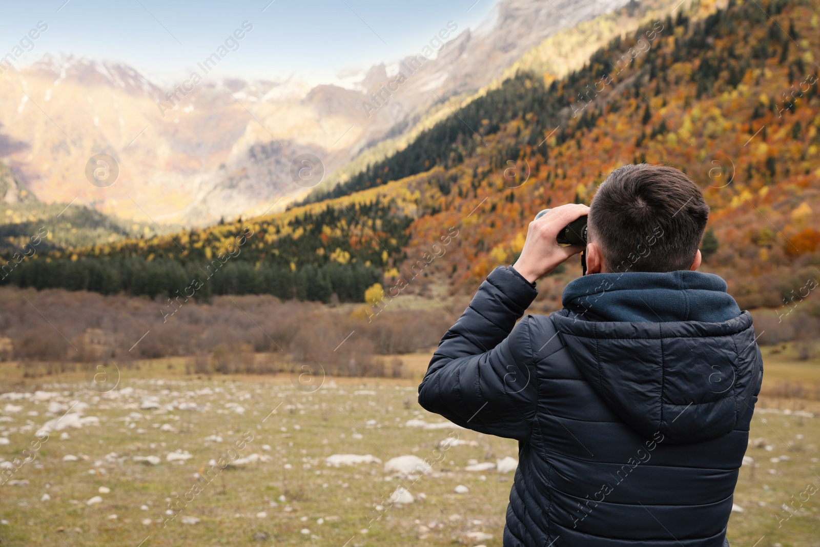 Photo of Boy looking through binoculars in beautiful mountains, back view. Space for text