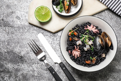 Delicious black risotto with seafood served on light grey table