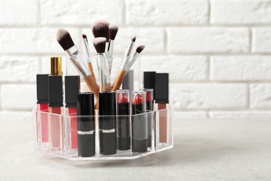 Photo of Lipstick holder with different makeup products on table against brick wall. Space for text
