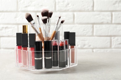 Lipstick holder with different makeup products on table against brick wall. Space for text